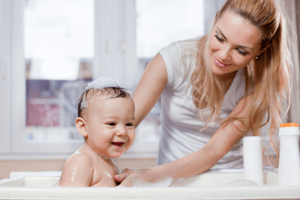 Bebê se diverte na hora do banho. Mamãe repleta de felicidade. Foto: Reprodução /  Canva