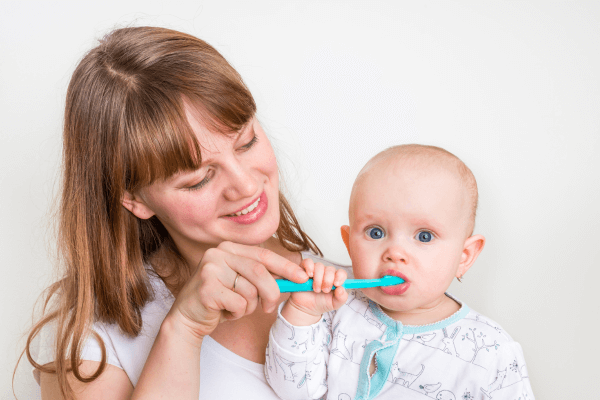 Mãe utilizando escova de dente para limpar os dentinhos do bebê. Foto: Reprodução /  Canva