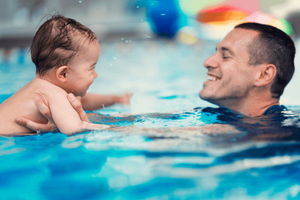 Pai interagindo com filho bebê durante aula de natação. Foto: Reprodução / Canva