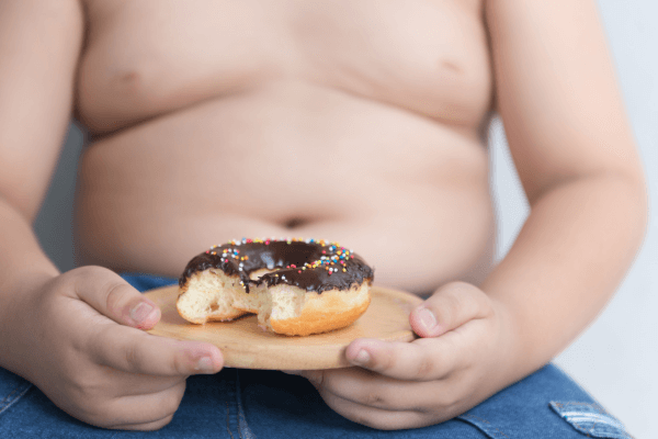 Criança obesa comendo uma rosquinha doce. Foto: Reprodução / Canva